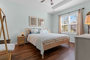 Een slaapkamer met een houten bed, twee nachtkastjes, een hangstoel en een raam met gordijnen.