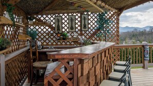 A wooden deck with a bar area, seating, and a view of mountains. - Poolside ADU w Sauna  Free Tix  Tiki Bar Retreat (Candler)