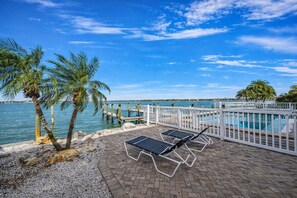 A poolside area with lounge chairs, a white fence, and palm trees. - Waterfront Condo | Heated Pool, Fishing Dock, Boat Slips & Walk to Beach (Treasure Island)