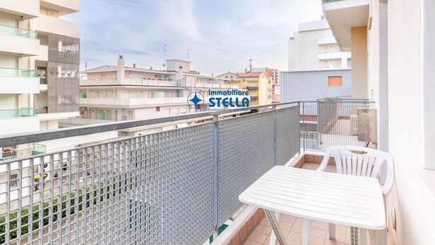 Un balcon avec une table et des chaises, une clôture et une enseigne indiquant « Immobiliare Stella ».