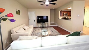 A living room with a sofa, TV, ceiling fan, and a kitchen area visible through an open door. - Spacious 3BR Near AT&T Stadium-Global Life Field-Texas Live!-FIFA WorldCup2026 (Arlington)