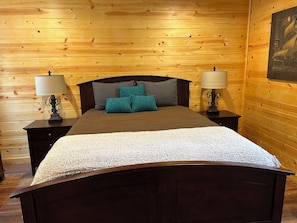 A wooden-paneled room with a bed, two bedside tables with lamps, and a wall-mounted artwork. - Terrific 3-bedroom cabin with AC in cozy Fish Camp (Fish Camp)