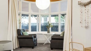 A room with a large window, two leather sofas, a white table, and a hanging decoration. - Esplanade Apartments Wavecaps (Dunedin)