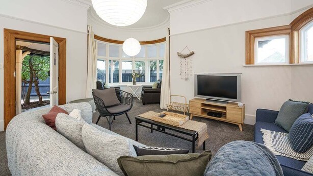 A living room with a sofa, armchair, TV, and a large window. - Esplanade Apartments Wavecaps (Dunedin)