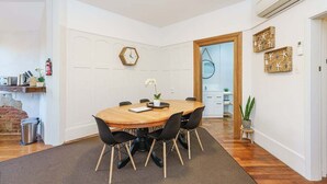 A dining area with a wooden table, black chairs, a clock, and a small potted plant. - Esplanade Apartments Wavecaps (Dunedin)