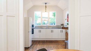 A kitchen with white cabinets, a wooden floor, and a window with a view of greenery. - Esplanade Apartments Wavecaps (Dunedin)