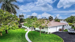 A single-story house with a red-tiled roof, surrounded by lush green lawns and palm trees.