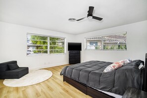 A modern bedroom with a bed, a black TV, a ceiling fan, and large windows.