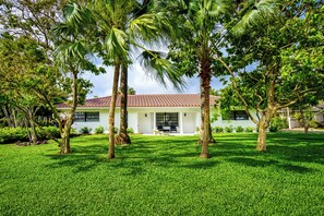 A house with a red-tiled roof, surrounded by a well-maintained lawn and palm trees.