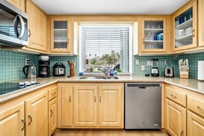 A kitchen with wooden cabinets, a dishwasher, a microwave, and a window with blinds.