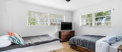 Un dormitorio con dos camas, un ventilador de techo, un televisor y ventanas amplias.