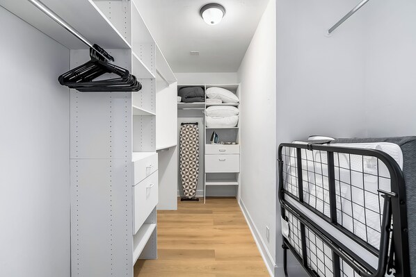Un couloir étroit avec des meubles de rangement blancs, un rideau à motifs et un cadre de lit en métal.