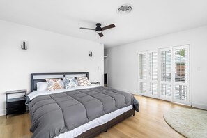 Ein modernes Schlafzimmer mit Bett, Nachttisch, Deckenventilator und Blick durch eine Glastür.