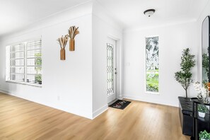 A spacious room with wooden flooring, a white door with a decorative glass panel, and a black doormat with 'Welcome' written on it.