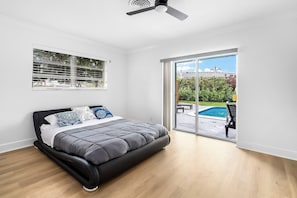A bedroom with a bed, a ceiling fan, a window with blinds, and a view of a pool.