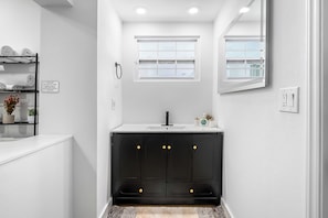 A modern bathroom with a white vanity, black cabinets, a window, and a towel rack.