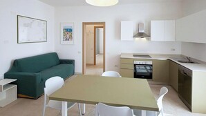 Un ambiente compatto con angolo cottura, un tavolo da pranzo con sedie, un divano verde e opere d'arte alle pareti.