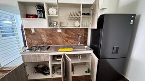 A compact kitchen with a gas stove, sink, and a black refrigerator. - CASA LUCY ALOJAMIENTOS (Palmira)
