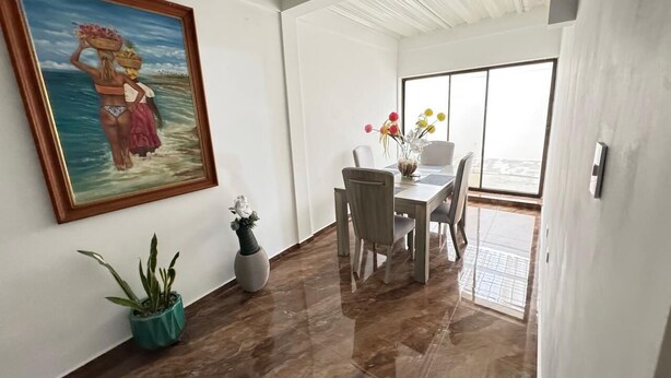 A dining area with a table and chairs, a painting on the wall, and potted plants. - CASA LUCY ALOJAMIENTOS (Palmira)