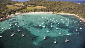 An aerial view of a coastal area with numerous sailboats anchored in clear turquoise waters, surrounded by lush green hills and a sandy beach. - Studio with terrace for 2 people in Giens – Secure residence near the beaches (HYERES)