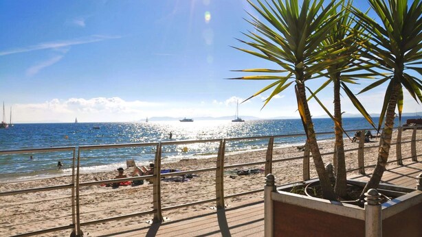 A beach with a wooden deck, palm trees, and the ocean. - Studio with terrace for 2 people in Giens – Secure residence near the beaches (HYERES)