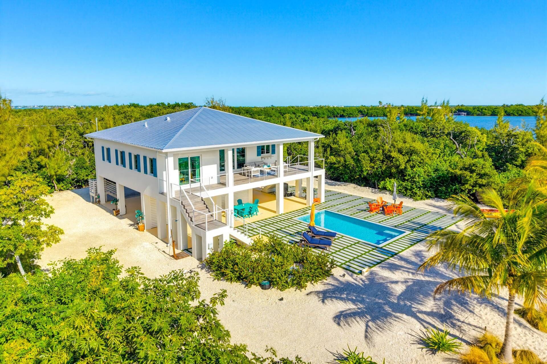 A two-story house with a pool, surrounded by trees and a beach.