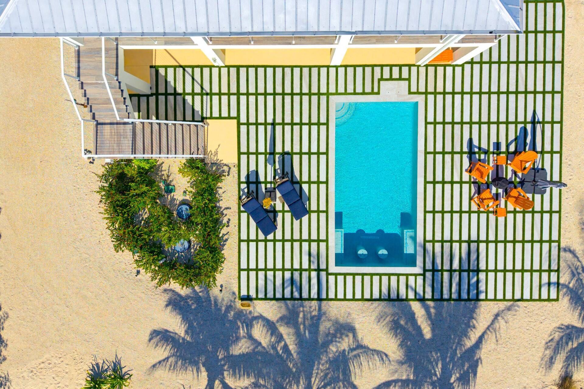 An aerial view of a resort with a swimming pool, lounge area, and a staircase leading to an upper level.