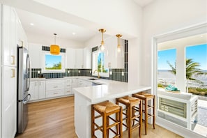 Una cocina moderna con armarios blancos, una isla grande con taburetes de bar y vista a la playa.