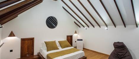 Un dormitorio con cama tipo loft, vigas de madera, un adorno circular en la pared y un sillón de peluche.