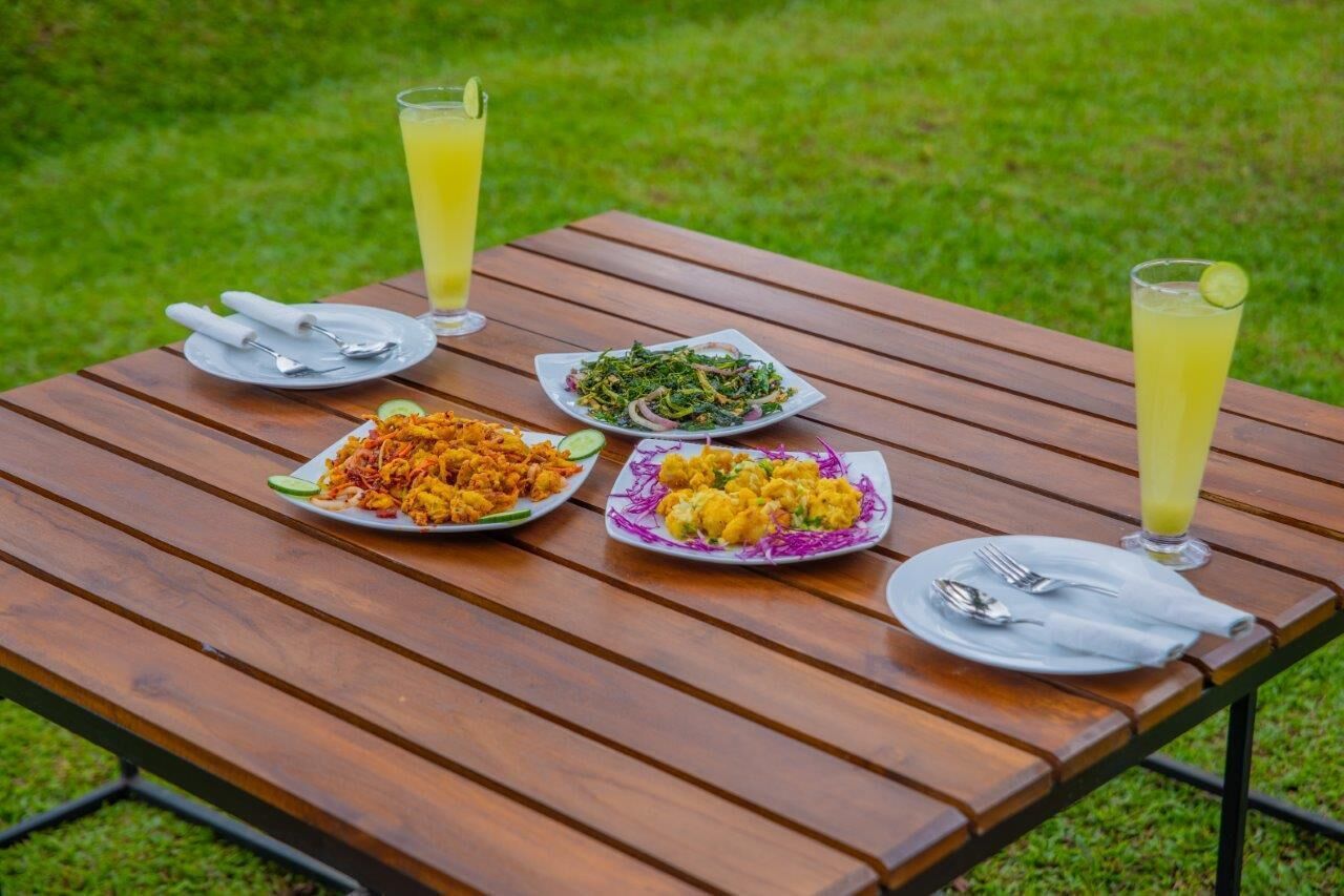 Una mesa de madera con platos de comida y bebidas, colocada al aire libre sobre césped.