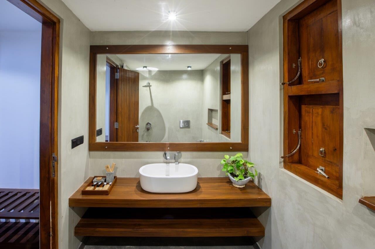 A modern bathroom with a large mirror, wooden vanity, and a shower visible in the reflection.