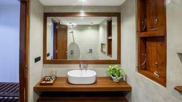 A modern bathroom with a large mirror, wooden vanity, and a shower visible in the reflection.