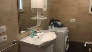 Ein kleines Badezimmer mit Waschbecken, Spiegel und Waschmaschine.