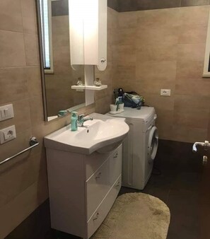 Ein kleines Badezimmer mit Waschbecken, Spiegel und Waschmaschine.