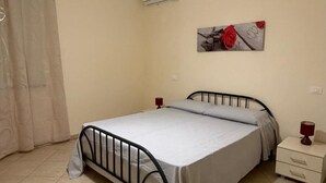 Ein Schlafzimmer mit einem Bett, einem Nachttisch, einer Lampe, einer Wand-Klimaanlage und einem Gemälde.