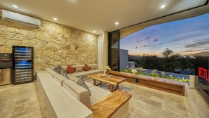 Uma sala de estar moderna com parede de pedra, um sofá, uma mesa de centro e uma grande janela com vista para o céu.