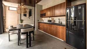 A modern kitchen with a dining area, wooden cabinets, a black refrigerator, and a hanging light fixture. - Siwa Jungle-Luxury 2BR Retreat with Private Rooftop, Deep Pool & BBQ (Tulum)