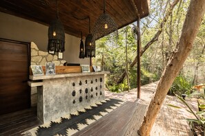 Un espace extérieur aménagé dans un style rustique, avec un comptoir en pierre, des lampes suspendues et des tableaux encadrés.