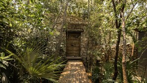 A stone archway leading to a wooden door, surrounded by dense tropical foliage. - Siwa Jungle-Luxury 2BR Retreat with Private Rooftop, Deep Pool & BBQ (Tulum)