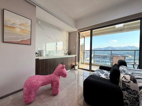 Una sala de estar moderna con un ventanal grande, una zona de cocina y un balcón con vistas a la ciudad.