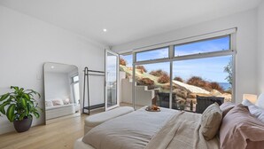 A bedroom with a large bed, a mirror, a potted plant, and a view of a coastal landscape through large windows. - Sunset Hideaway in Marino (Marino)