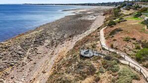 A coastal area with a rocky beach, a paved walkway, and a small structure with a railing. - Sunset Hideaway in Marino (Marino)