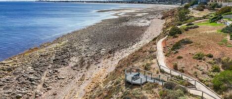 Une zone côtière avec une plage rocheuse, une promenade dallée et une petite construction dotée d’une rambarde.