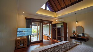 A bedroom with a bed, a TV, a desk, a mirror, and a view of the outside. - DENAYA UBUD VILLA (Ubud)