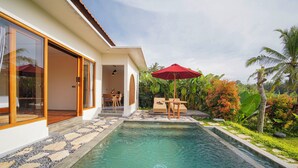 A swimming pool with a stone border, a wooden deck, and a red umbrella. - DENAYA UBUD VILLA (Ubud)