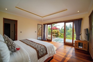 Quarto com uma cama grande, televisão e porta de vidro que se abre para um pátio.