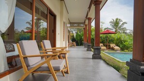 A covered outdoor area with wooden chairs and a pool. - DENAYA UBUD VILLA (Ubud)