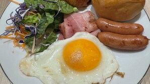 En tallrik med en croissant, en korv, ett stekt ägg och en sallad.