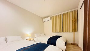 Ett hotellrum med två sängar, ett nattduksbord med en lampa, en luftkonditioneringsanläggning och en golvlampa.
