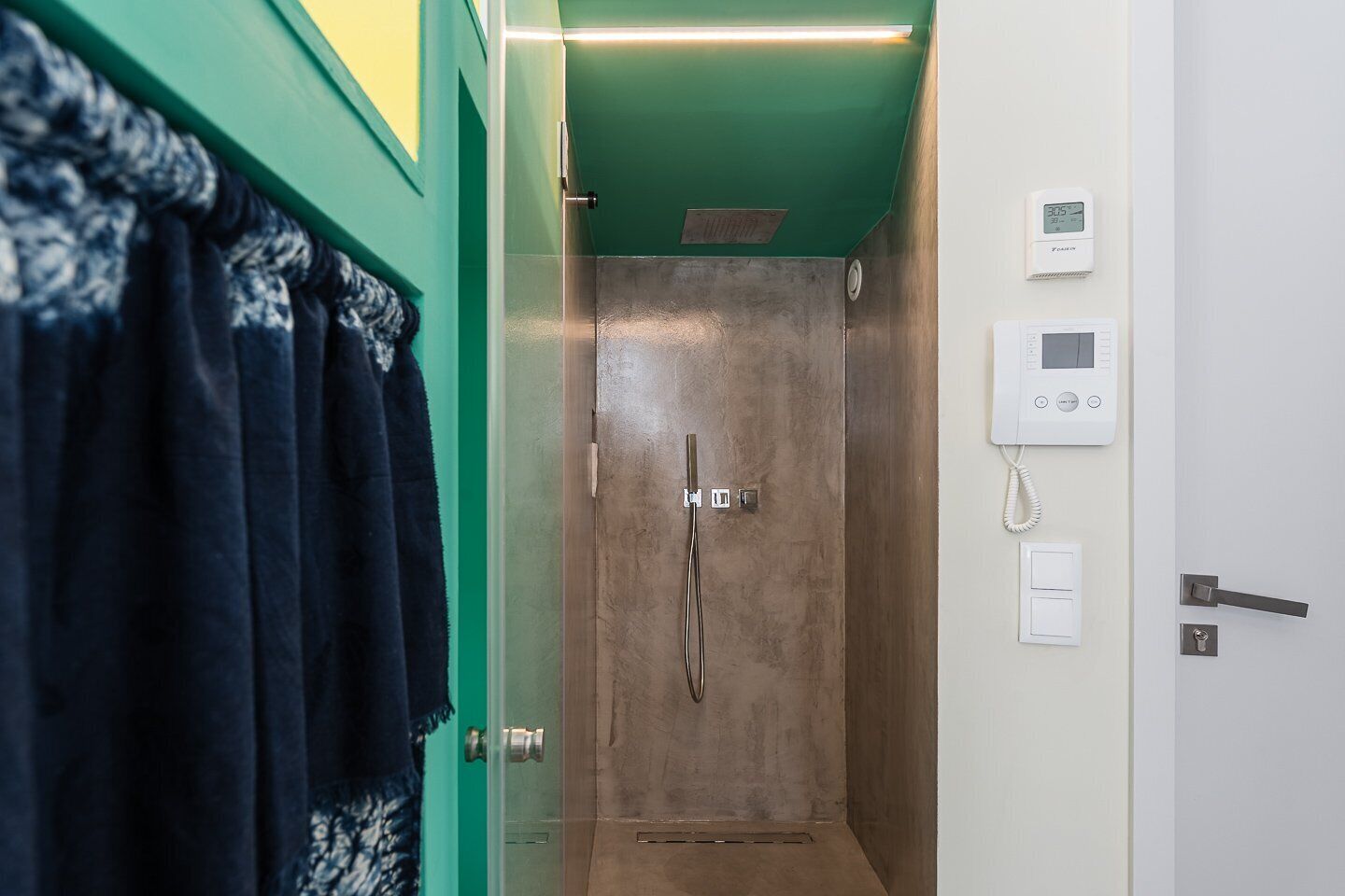 Un baño con ducha, un perchero con toalla, un termostato y un interruptor de luz en la pared.